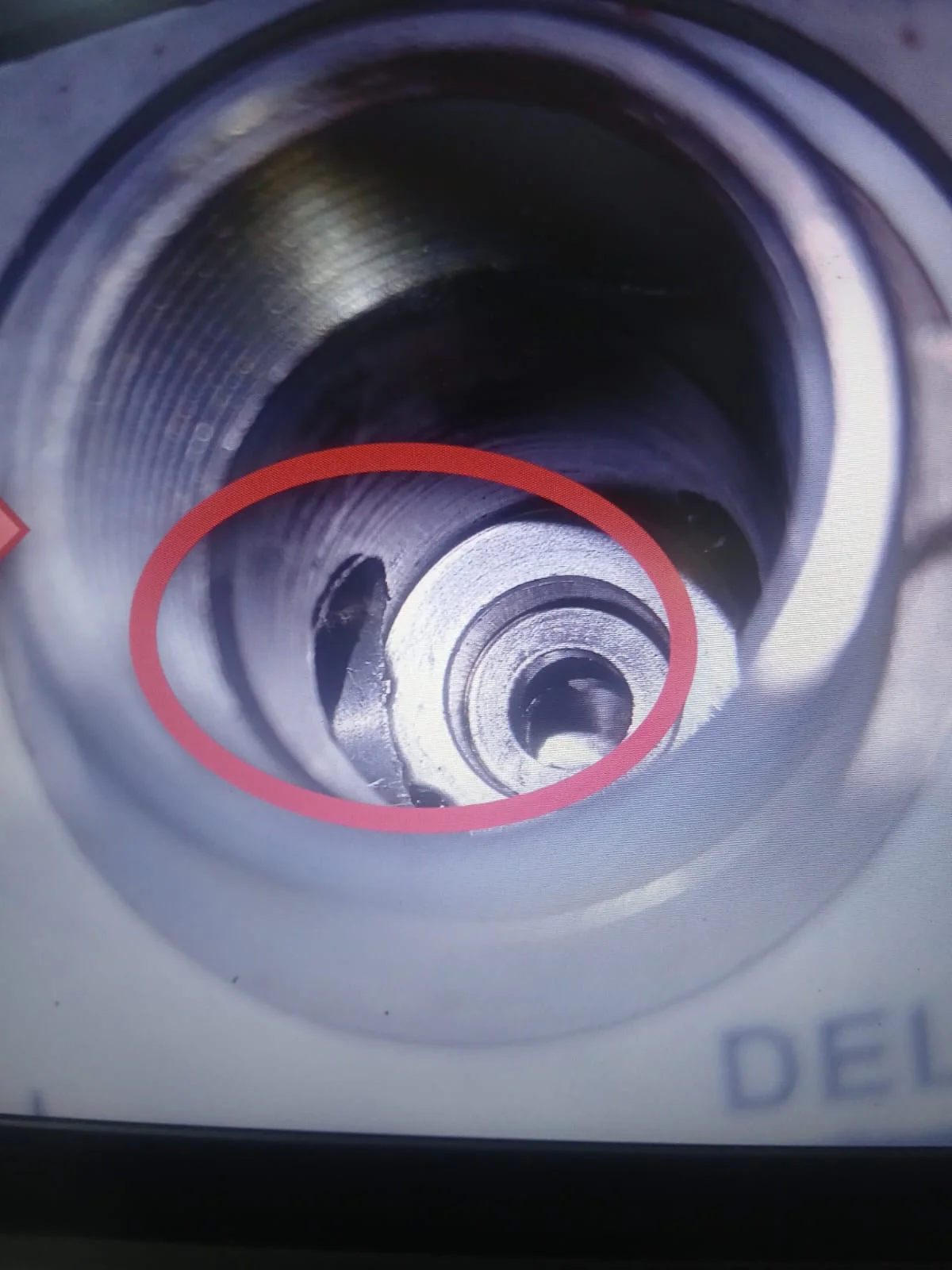 Magnified internal bore before deburring, with the cross-hole burr circled in red
